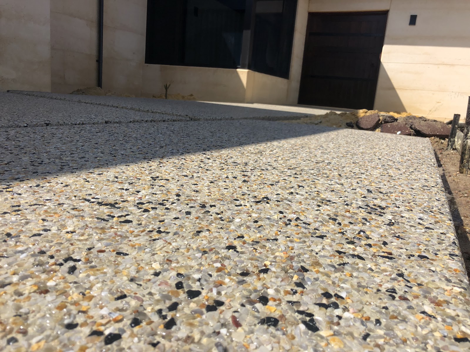 Exposed aggregate driveway panels drying at a rammed-earth home, stone detail up close