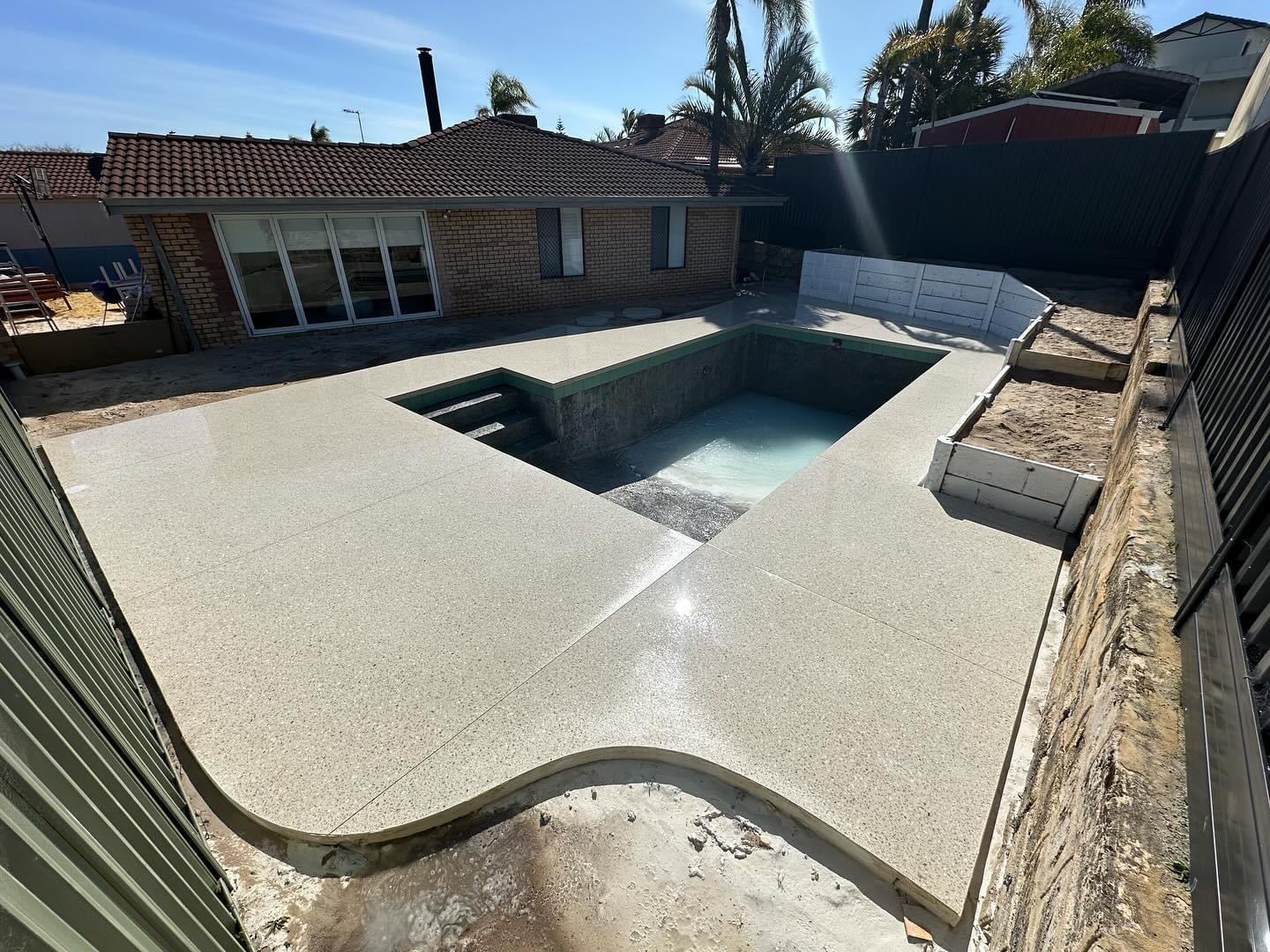 Honed concrete surround wrapping a renovated pool, steps formed into the shallow end
