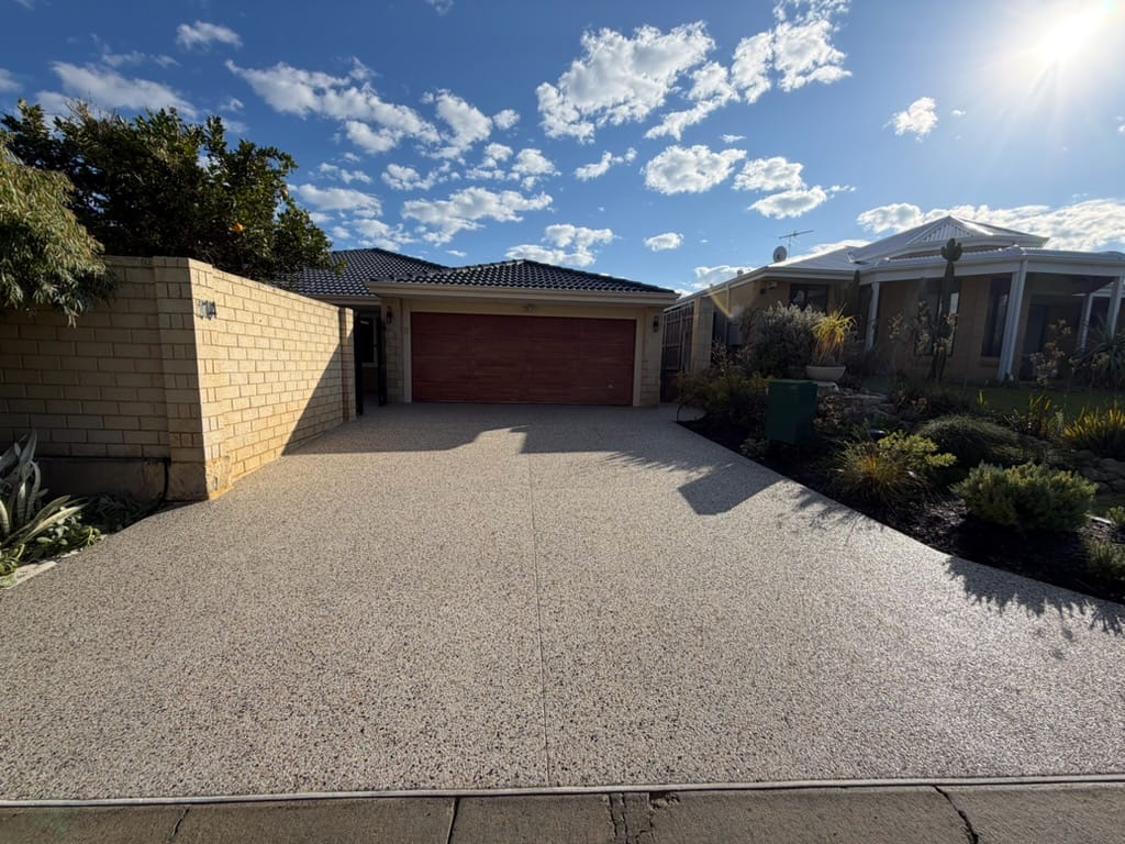 Exposed aggregate driveway at a single-storey home behind a limestone wall