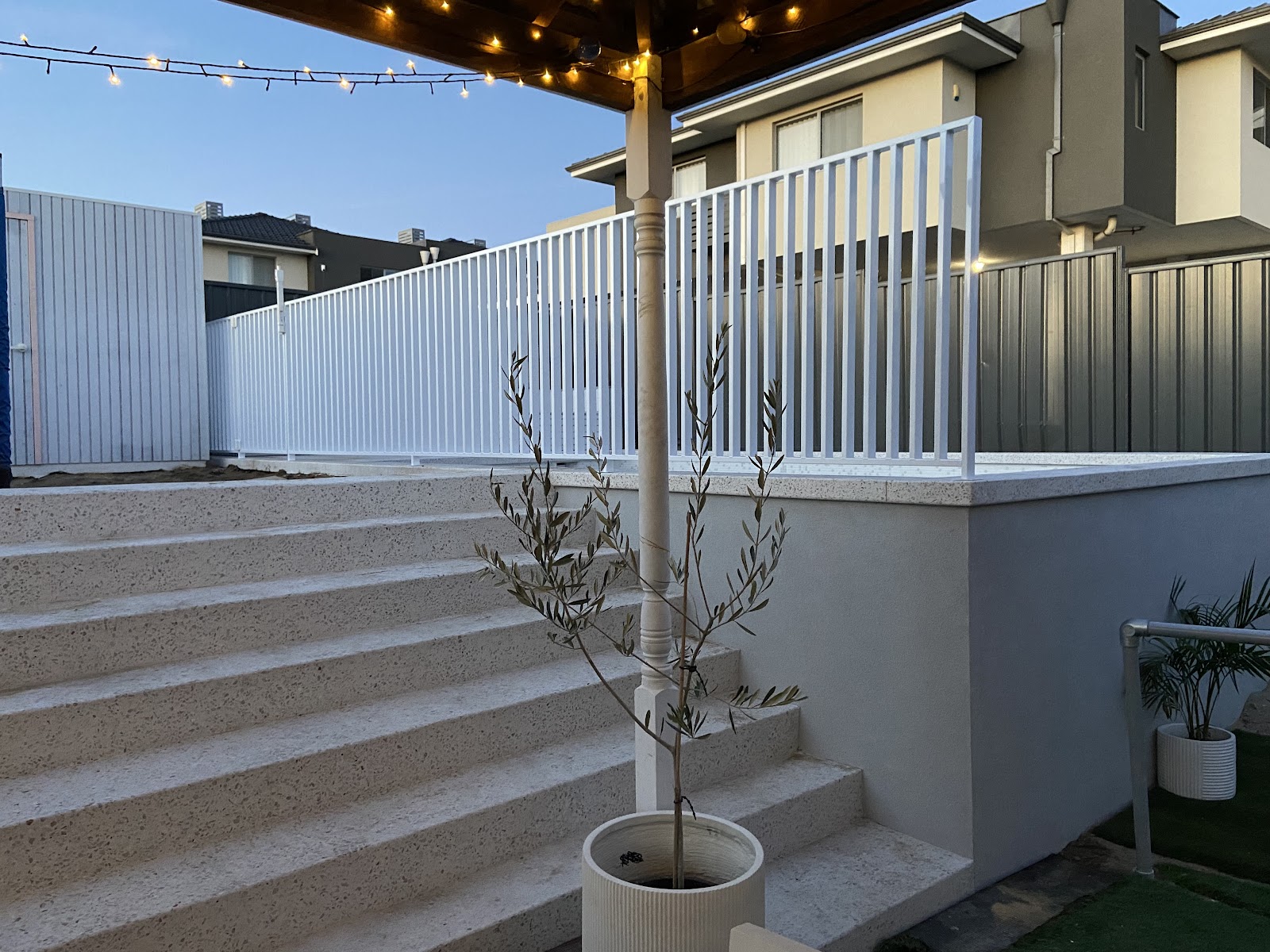 White honed steps and raised pool edge at dusk under festoon lights