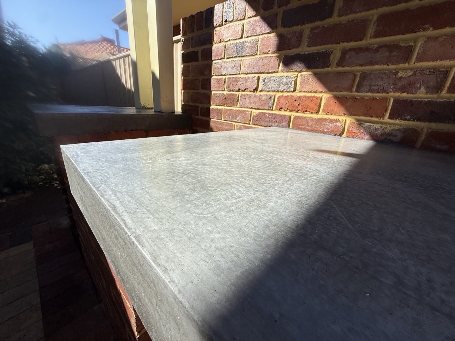 Burnished concrete benchtop with a crisp square edge, set against recycled red brick