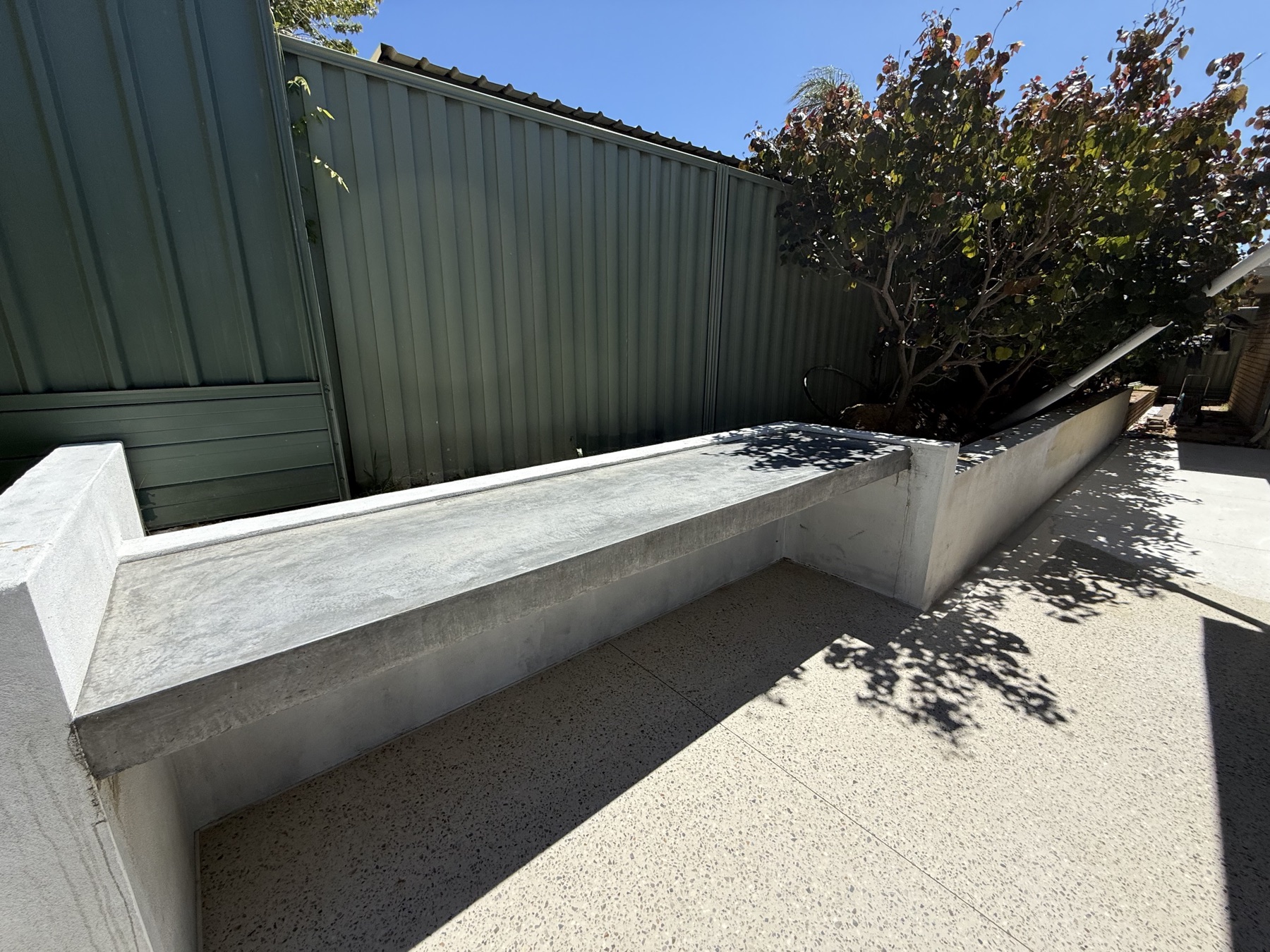 Long floating concrete bench beside a honed aggregate path, cast into the retaining wall