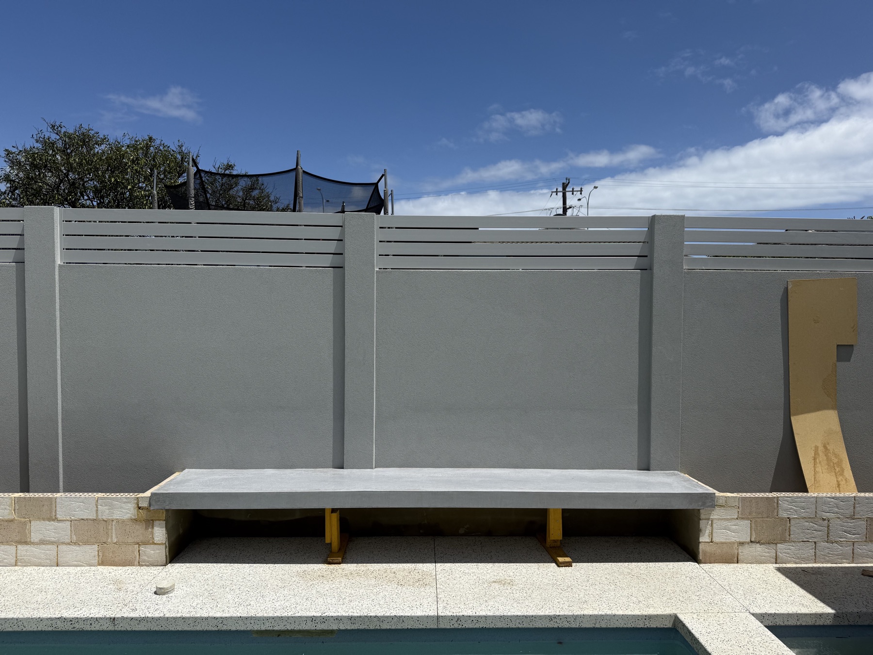 Floating concrete bench cast into a rendered pool wall above terrazzo-look paving
