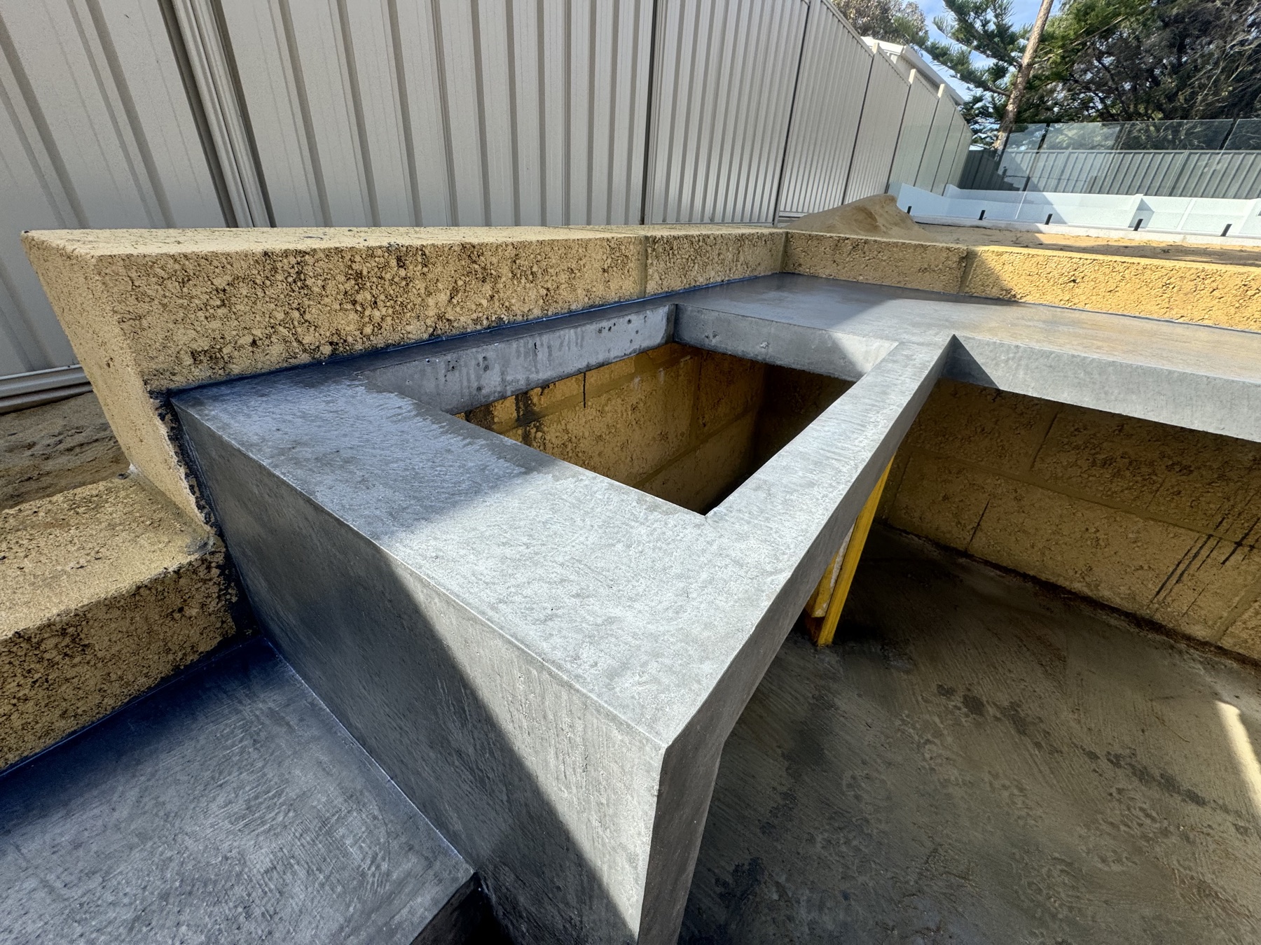 Charcoal concrete planter and bench detail at the pool corner, cast against limestone block