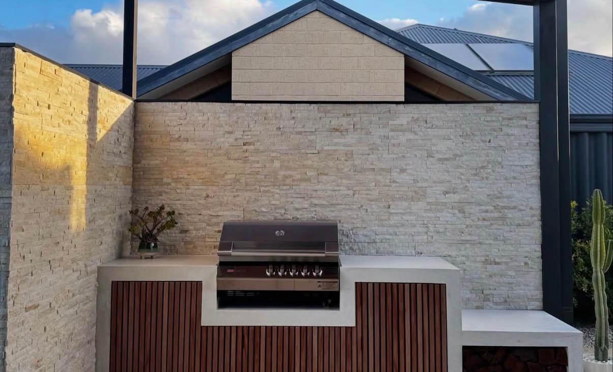 Front elevation of the outdoor kitchen, one concrete benchtop running the full width with timber slat doors below and a firewood store at the end