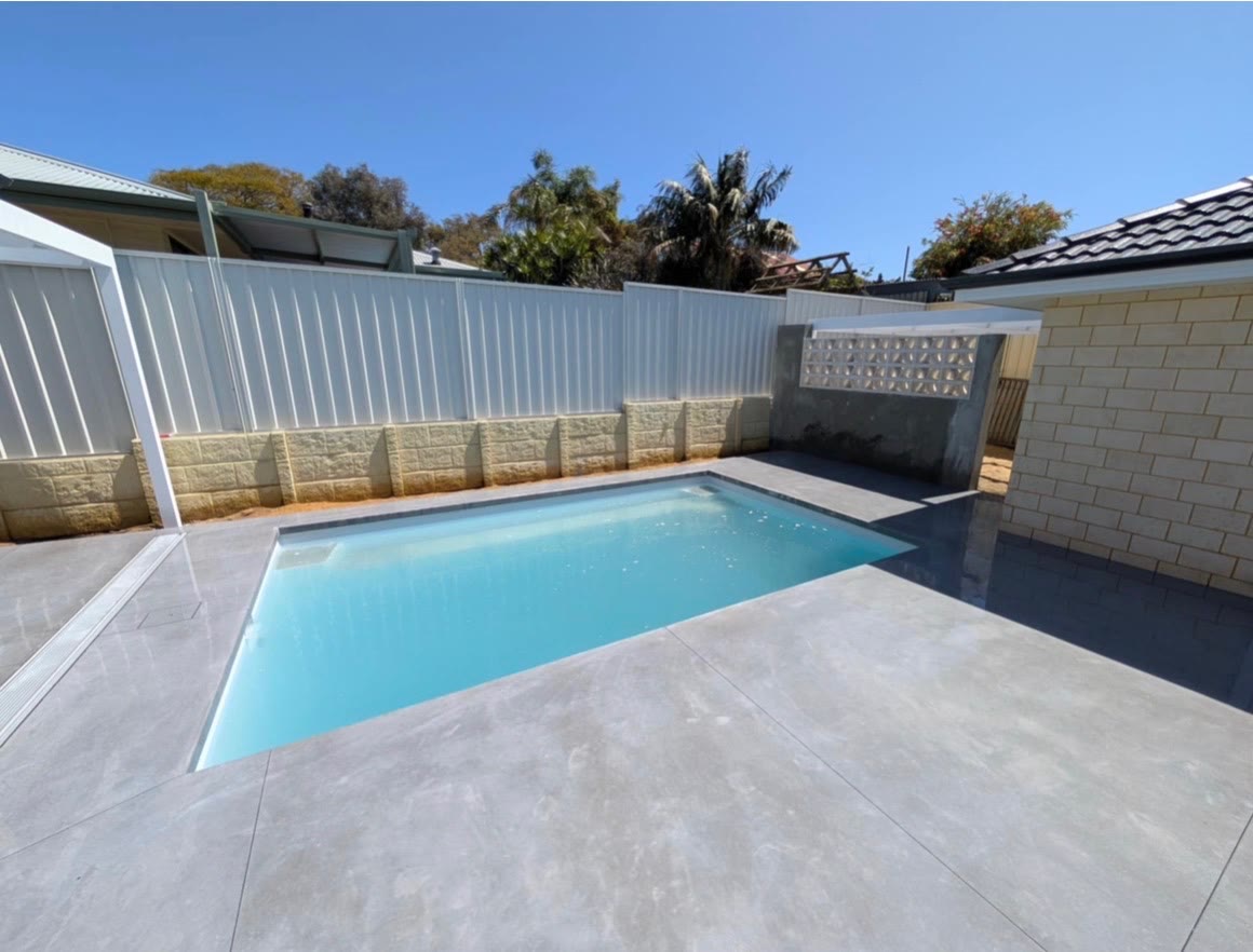 Honed concrete surround finished around a new pool, poured in wide bands out to the fence line